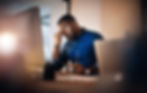 Man looking stressed while working on his computer, rubbing his eyes in frustration.