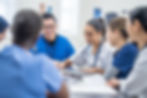 Group of healthcare workers in scrubs, smiling and collaborating around a table during a team meeting