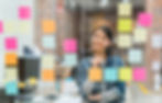 Woman brainstorming with colorful sticky notes on a glass wall, planning and organizing ideas in an office.