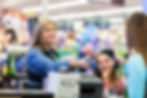 A customer smiling to the cashier while holding a baby at the checkout.