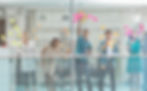 Five colleagues writing and posting post-its on a transparent wall