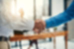 Two people shaking hands in an office setting, suggesting a professional agreement or greeting.