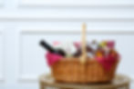 A festive gift basket filled with wine, chocolates, and other treats on a home coffee table.