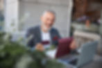 Happy mature man using a credit card and laptop to redeem a gift card online at an outdoor cafe.