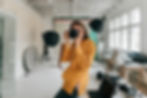 A photographer in a yellow sweater taking a picture in a well-equipped studio with professional lighting equipment.