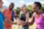 Four diverse individuals sharing a joyful moment outdoors, stacking hands and smiling after exercise.