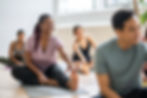 A yoga instructor smiles during a session with a diverse group of participants in a sunlit studio.