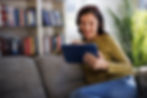 A woman sitting in the sofa with headphones on and using her tablet
