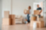 Young couple moving boxes into a new home, with a dog by the door.