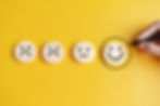 Wooden round icons showing different emotions with a hand drawing a circle around a happy face.