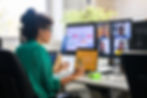 Woman in a green blouse attending a video conference call with colleagues on large monitors in an office