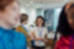 Networking event with professionals in casual attire engaging in conversations, wearing lanyards in a bright conference space