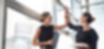 Two businesswomen high-fiving each other in an office with large windows.