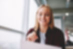 A smiling woman reviewing a document while sitting in a bright office space with large windows.