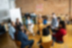 A diverse group of people sitting in a circle, engaged in a discussion in a casual workspace.
