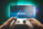 Hands holding a game controller with a blurred gaming screen in the background.