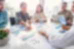 A diverse team in a modern office, reviewing charts and graphs spread across a table, discussing data.