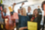 A vibrant office celebration with diverse team members cheering over a success with sticky notes on glass.