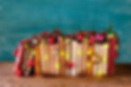 A row of books decorated with festive lights, ornaments, and miniature Christmas trees against a teal background.