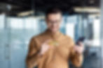 A man smiling while looking at his credit card and smartphone, preparing for an online purchase.