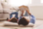 A child and an adult lying on the floor reading a book together in a cozy living room.