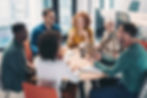 A diverse group of professionals engaged in a lively discussion around a round table in a modern office.