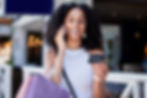 A woman talking on the phone looking at a gift card and holding shopping bags