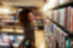 Happy young woman browsing books in a cozy bookstore.