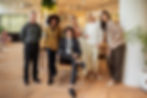 A well-dressed group of professionals posing confidently in a stylish office space with warm lighting and plants.