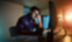 Man working late at a computer, looking tired and rubbing his eyes.