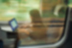 A woman working on her laptop during a train journey, with a blurred scenic view outside the window