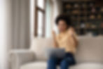 A woman celebrating with excitement while looking at her laptop on a couch.