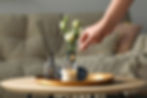Hand lighting a candle on a tray with a diffuser and flowers in a cozy living space.