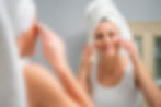 Woman applying facial cream in the bathroom, looking at mirror, smiling.