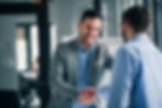 Two businessmen shaking hands and smiling, symbolizing agreement, partnership, or a positive meeting.