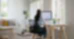 A woman focused on data analysis on her computer at a bright, plant-filled home office.
