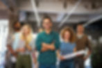 A diverse team of confident professionals smiling in an industrial-style office, holding documents and looking motivated.
