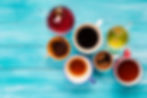 Variety of colorful teas and coffees in different cups on a vibrant wooden table.