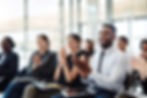 A group of smiling employees sitting and applauding during a presentation