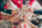Close-up of hands raising glasses for a toast during a festive gathering, with holiday decorations in the background.
