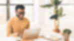 Cheerful man using laptop in a bright office with green plants.