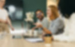 Colleagues engaging in a lively discussion during a meeting, with laptops and coffee cups.