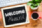 Chalkboard with 'Welcome Aboard' on a wooden desk with coffee and a plant