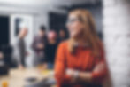 A woman looking to the side and smiling in the office, with colleagues standing in the background