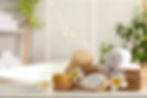 Basket with rolled towels, loofah, and spa products, surrounded by flowers in a serene spa setting.