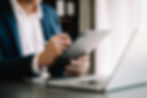 Businessperson using a digital tablet and stylus, working at a desk with a laptop in a professional setting.