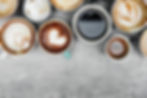 Top view of various coffee cups with different designs of froth art on a gray background.