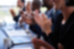 Diverse group of professionals clapping in a business meeting with laptops open.