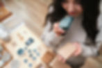 Blissful woman hands holding neat eco soap and a wooden soap dish. Smelling soap with a happy face. Overhead view. Standing in ecological shop in front of the table with variety of cosmetic items.