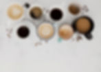Top view of several cups of coffee ranging from espresso to latte on a white background.